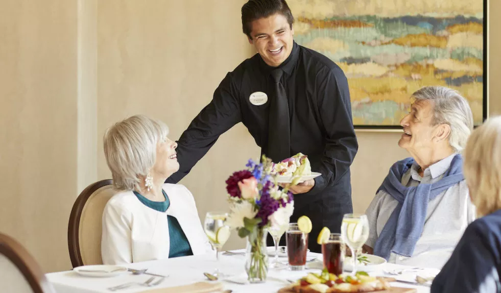 A smiling waiter serving a couple at a table