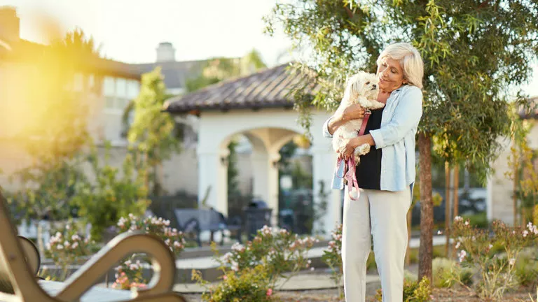 Senior lady holding a white middle size dog on her hands outside