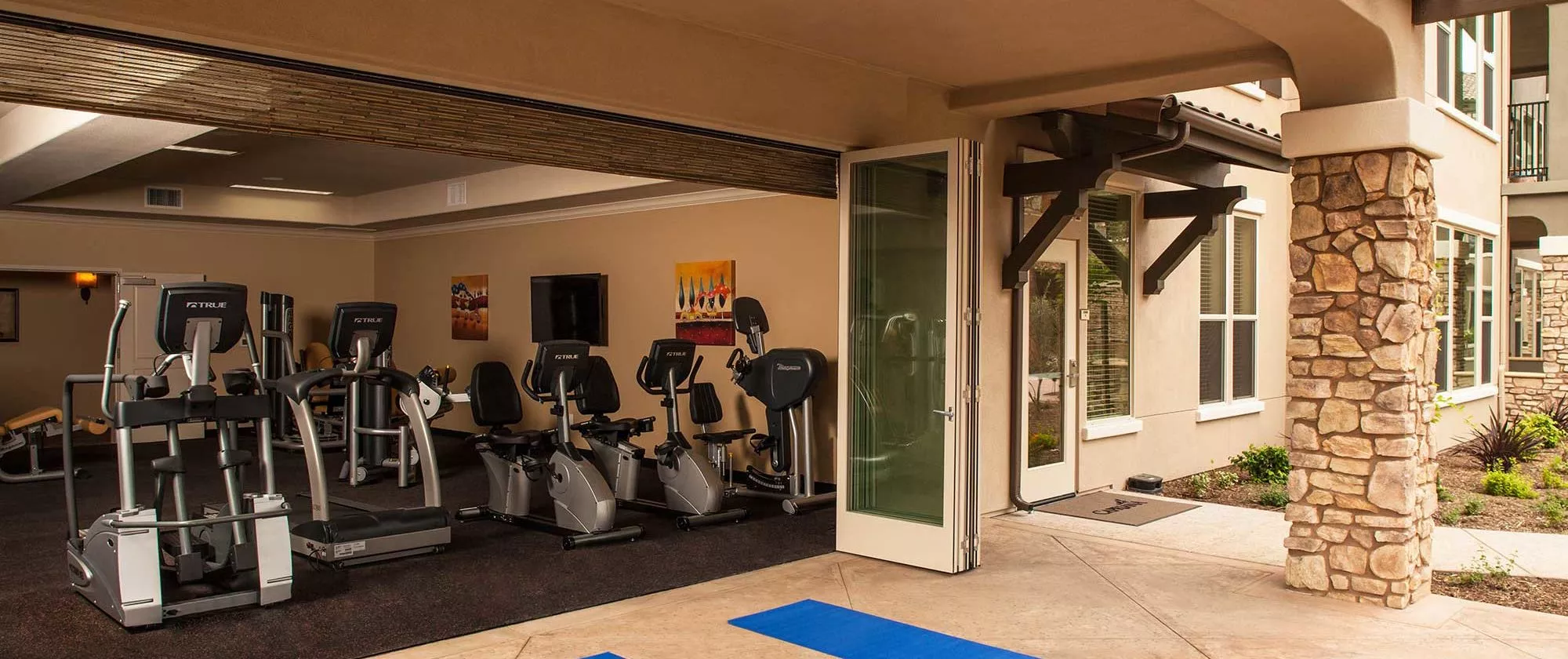 Capriana gym with open slide doors to patio where yoga mats and weights are set up for exercise