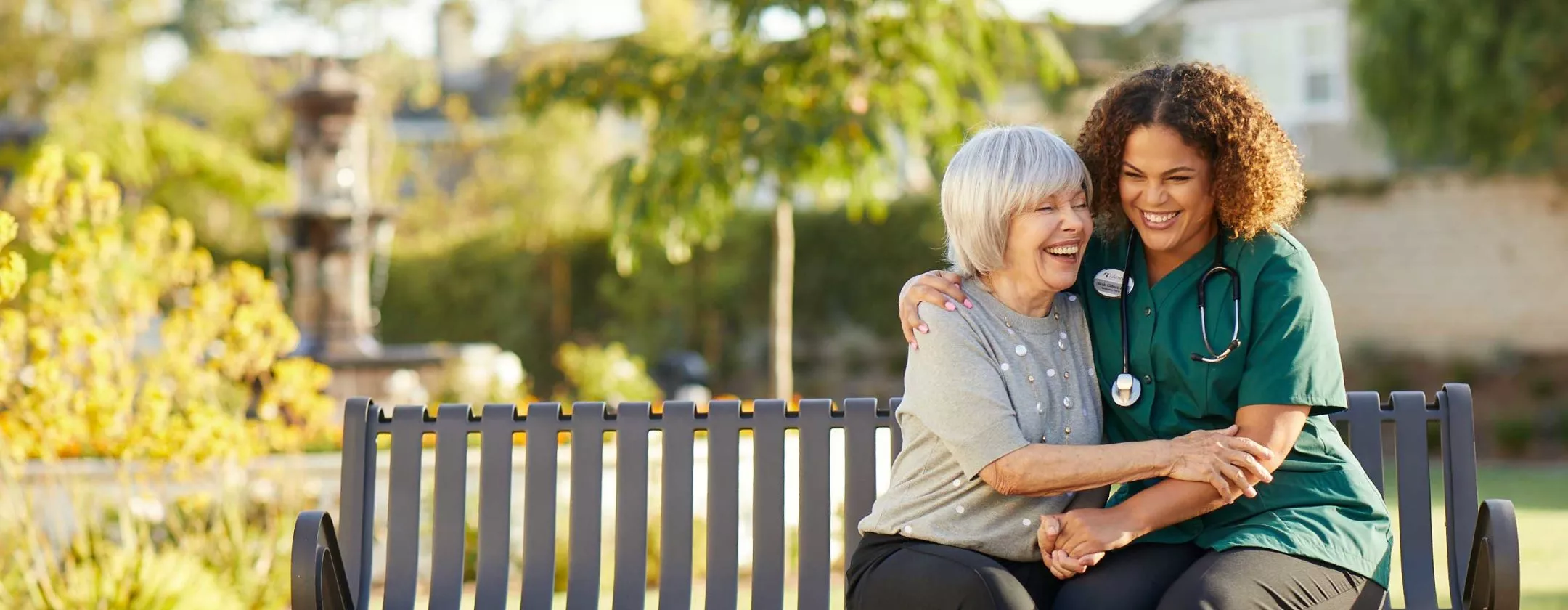 Caregiver is laughing with a senior lady on a bench