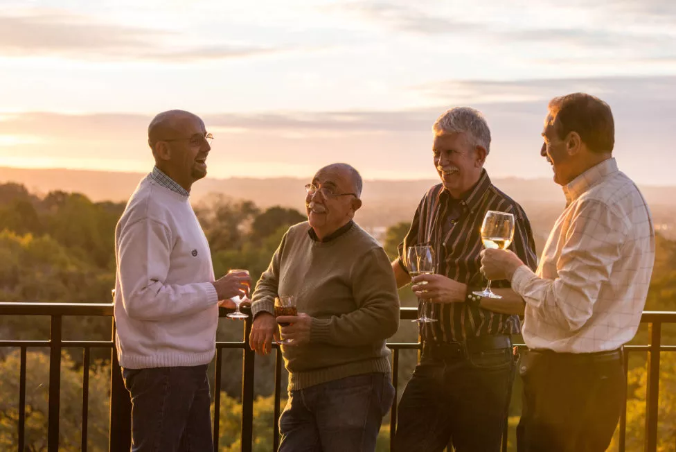 Four men having a drink on patio with beautiful view, laughing with each other
