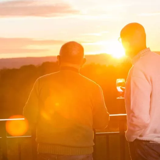 Two men having a drink and watching the sunset from patio with beautiful view