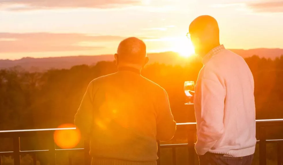 Two men having a drink and watching the sunset from patio with beautiful view