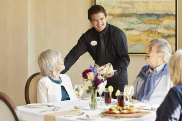 A smiling waiter serving a couple at a table