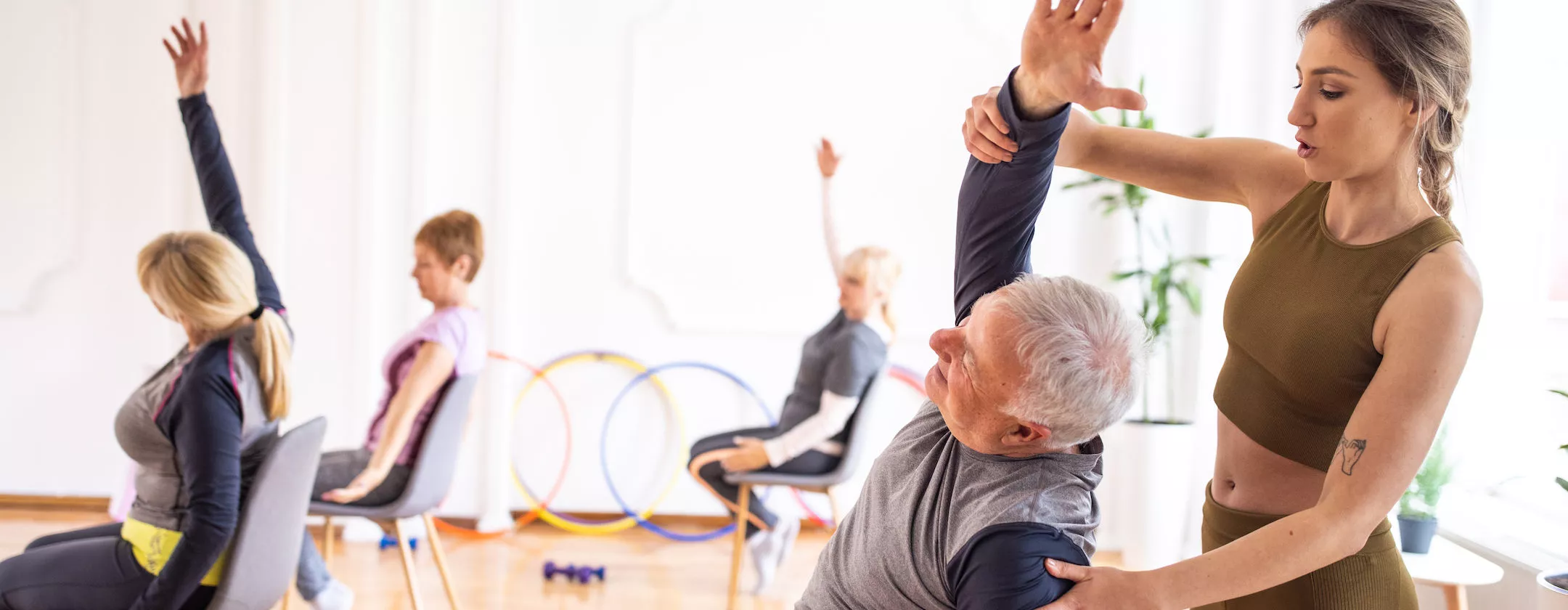 Yoga instructor assisting senior man during yoga class on chairs