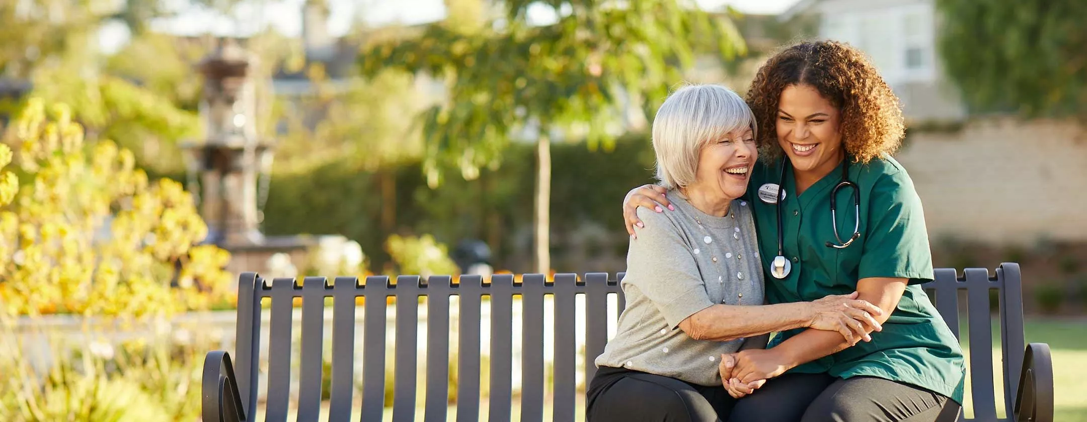 Caregiver is laughing with the senior lady on a bench
