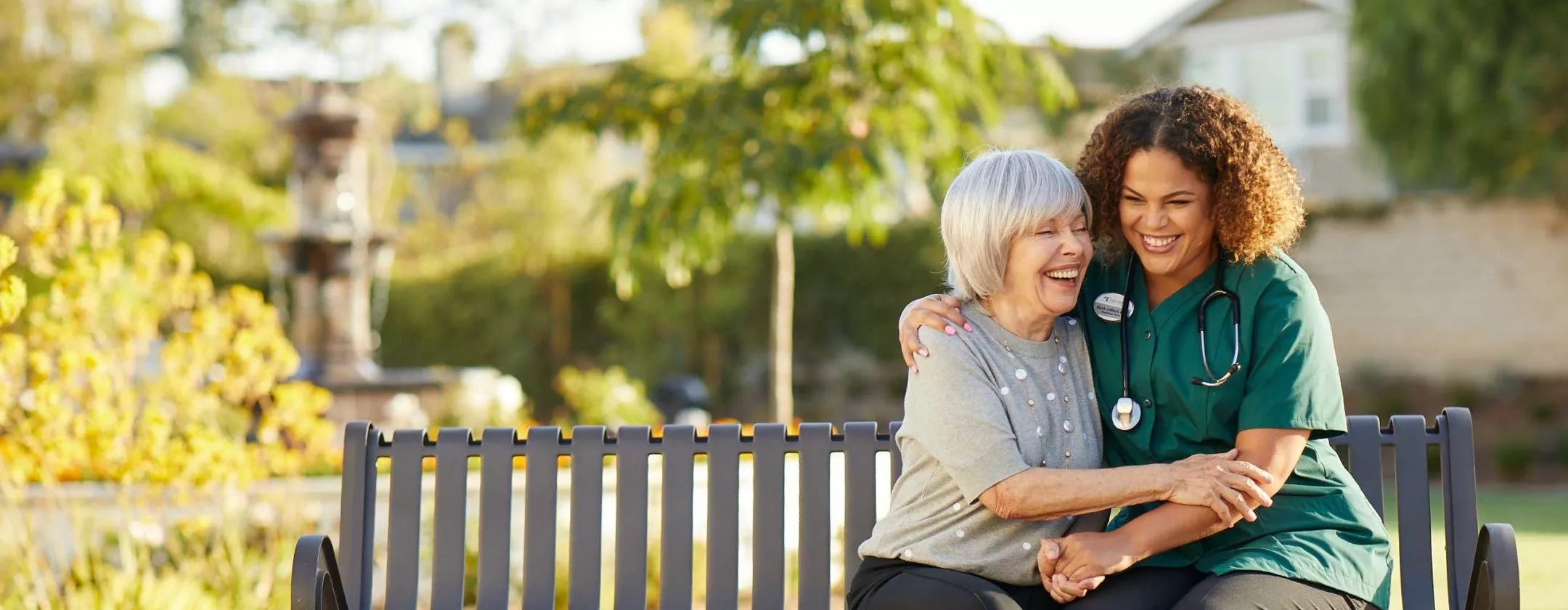 Caregiver is laughing with a senior lady on a bench