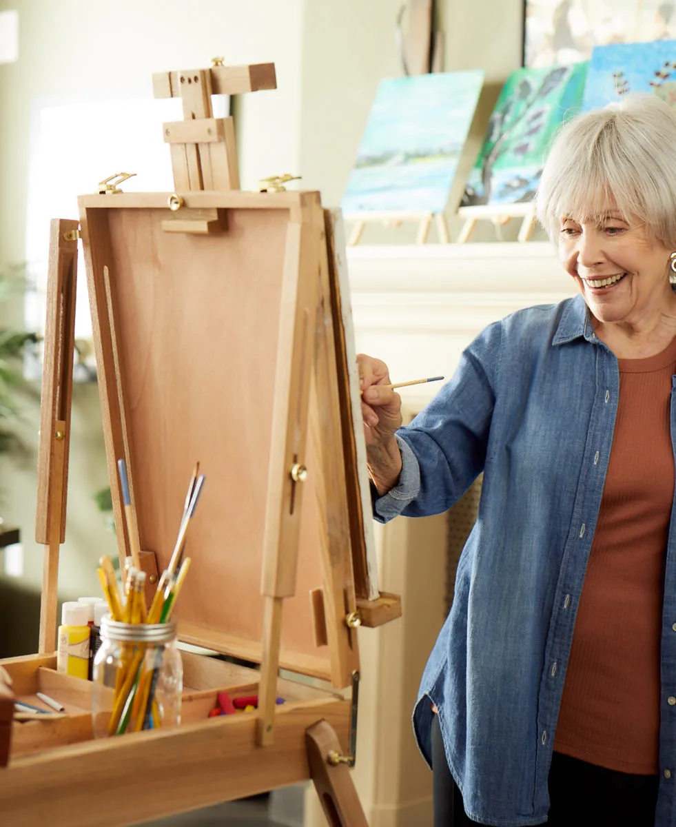 Senior lady is painting behind the easel