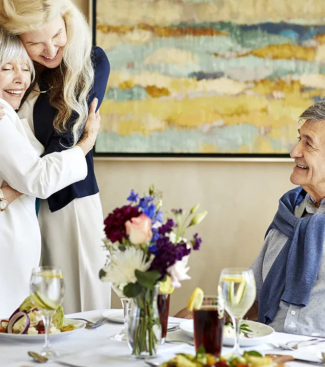 Caregiver is hugging a senior lady over the dining table