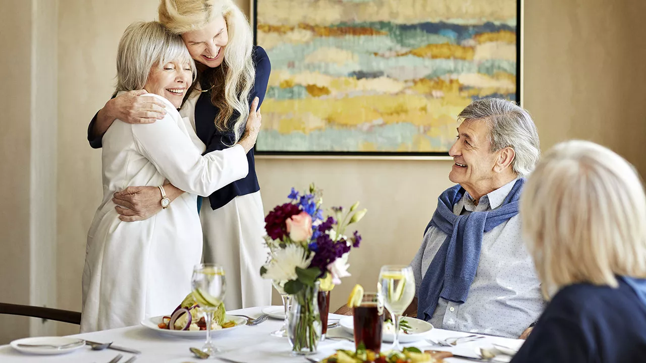 Caregiver is hugging a senior lady over the dining table