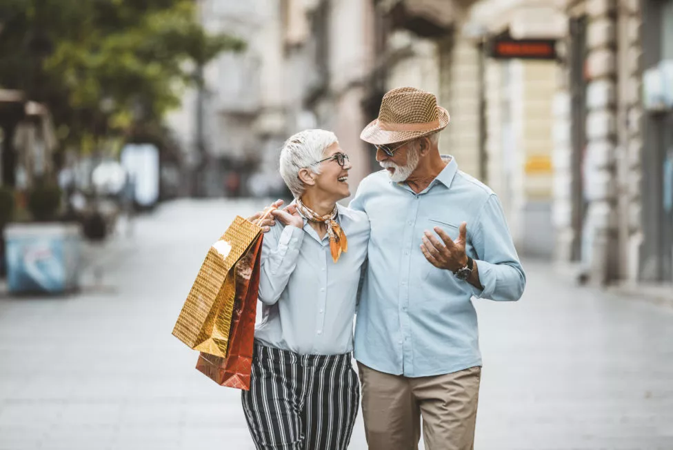 Middle aged men and women, walking arm in arm, looking at each other, laughing, women is holding shopping bags in her hand