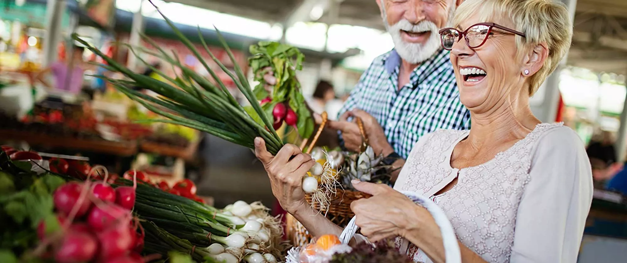 Middle aged man and woman buying onion and radish at store, laughing with each other