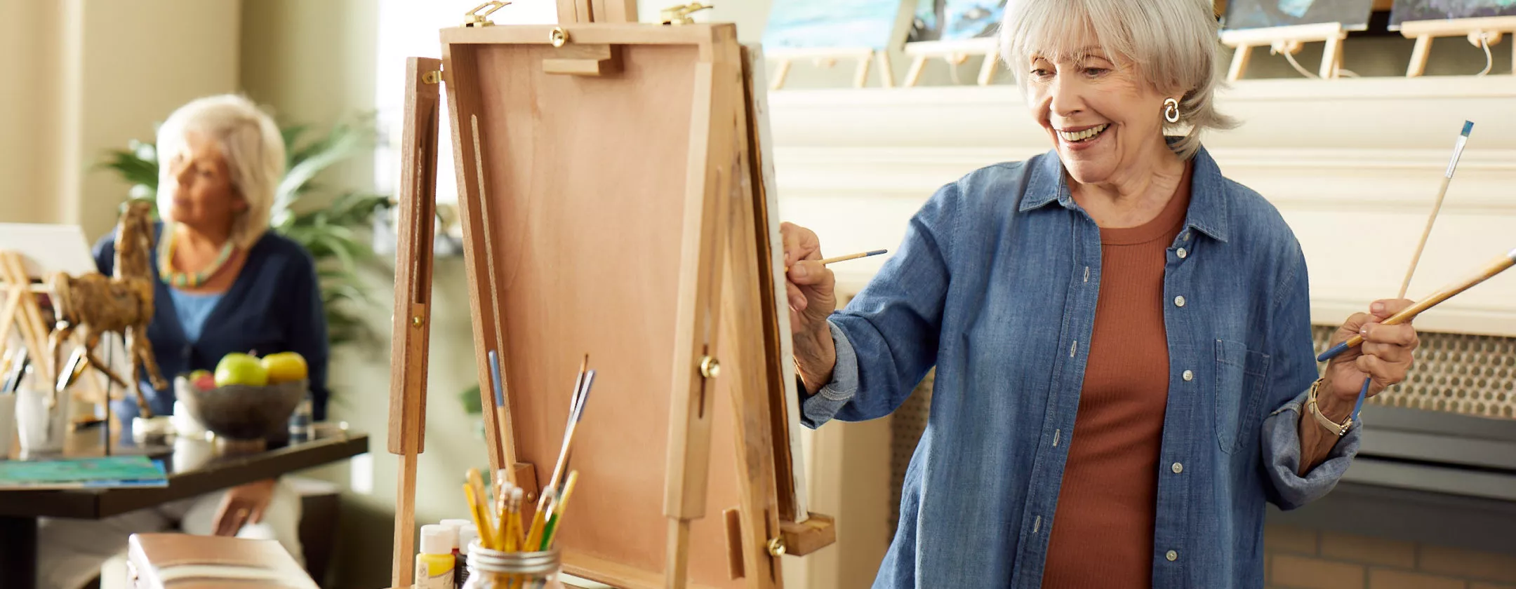 Senior lady is painting behind the easel