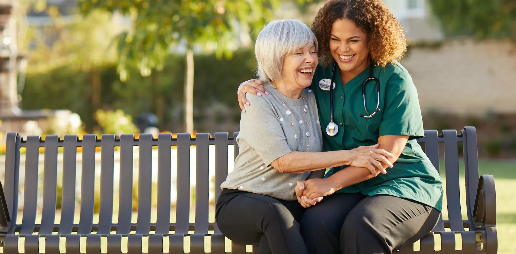 Caregiver is laughing with the senior lady on a bench