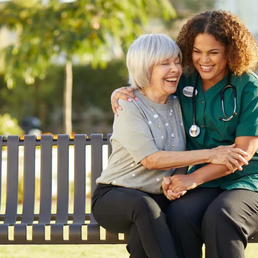 Caregiver is laughing with the senior lady on a bench