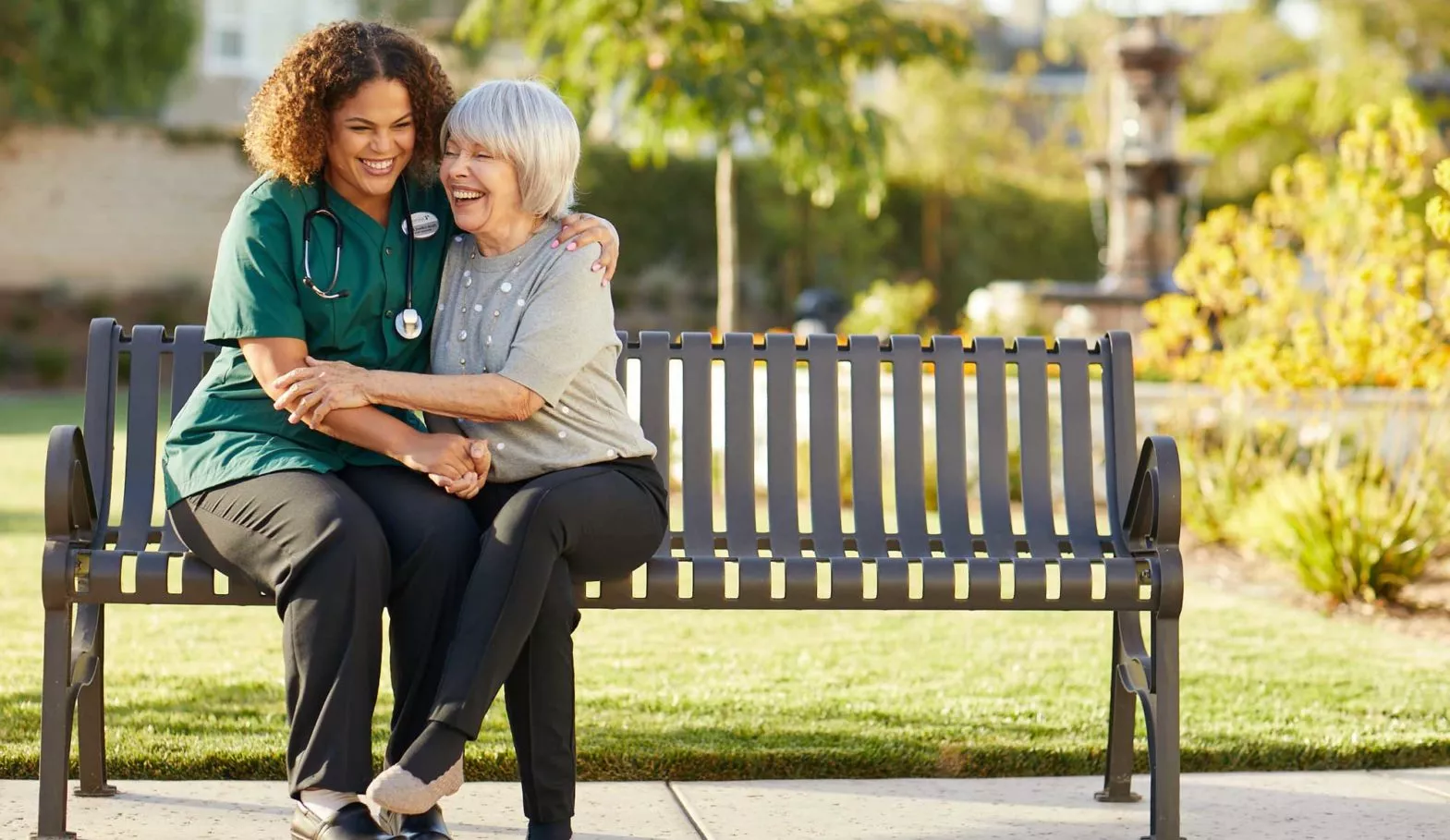 Caregiver embraces senior woman on a bench
