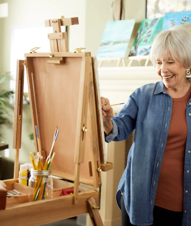 Senior lady is painting behind the easel