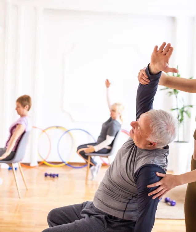Yoga instructor assisting senior man during yoga class on chairs