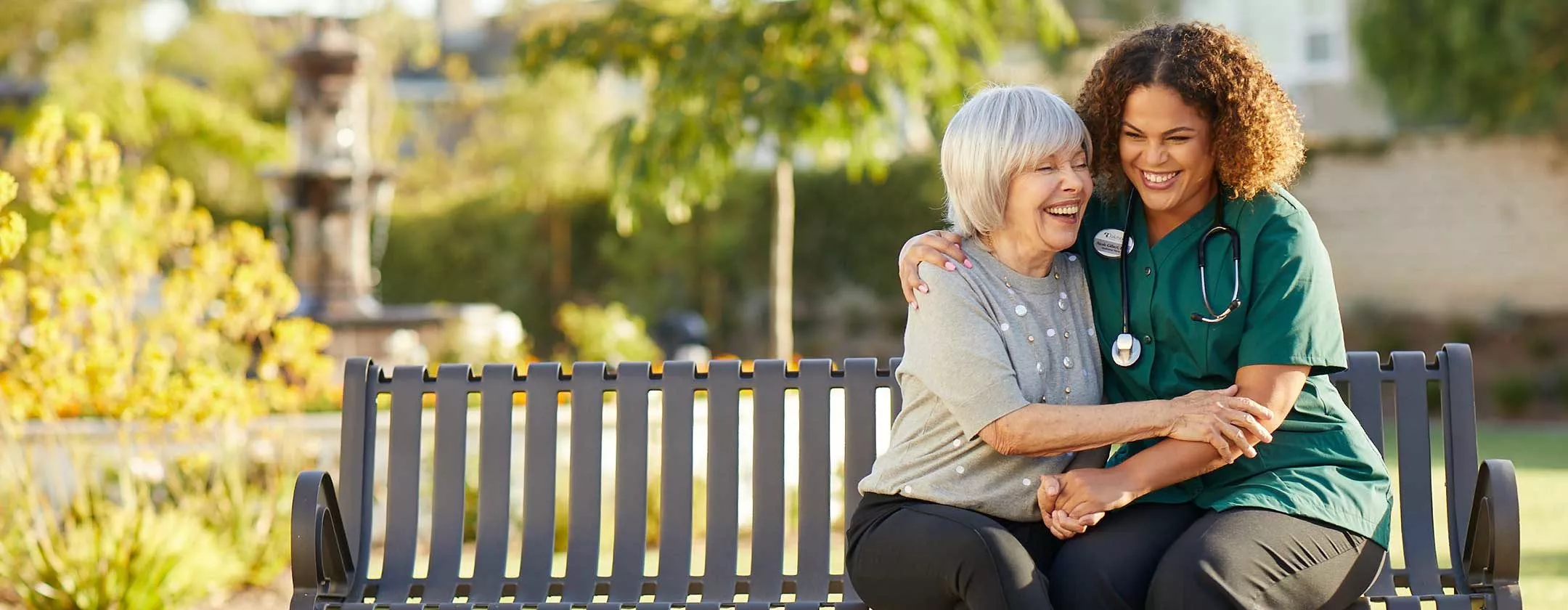 Caregiver embraces senior woman on a bench