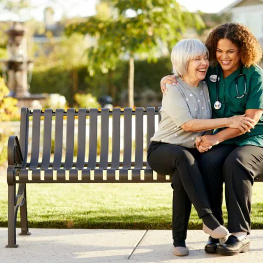 Caregiver embraces senior woman on a bench
