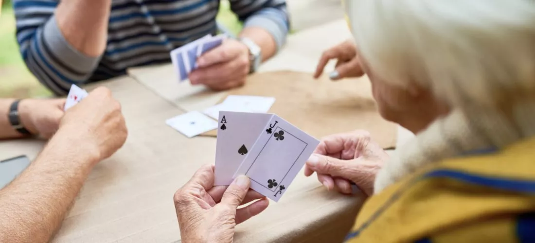 An elderly group of people playing cards, with one person holding an Ace of clubs and a Jack of spades.