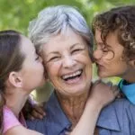 An elderly lady with two children on either side of her giving her a kiss.