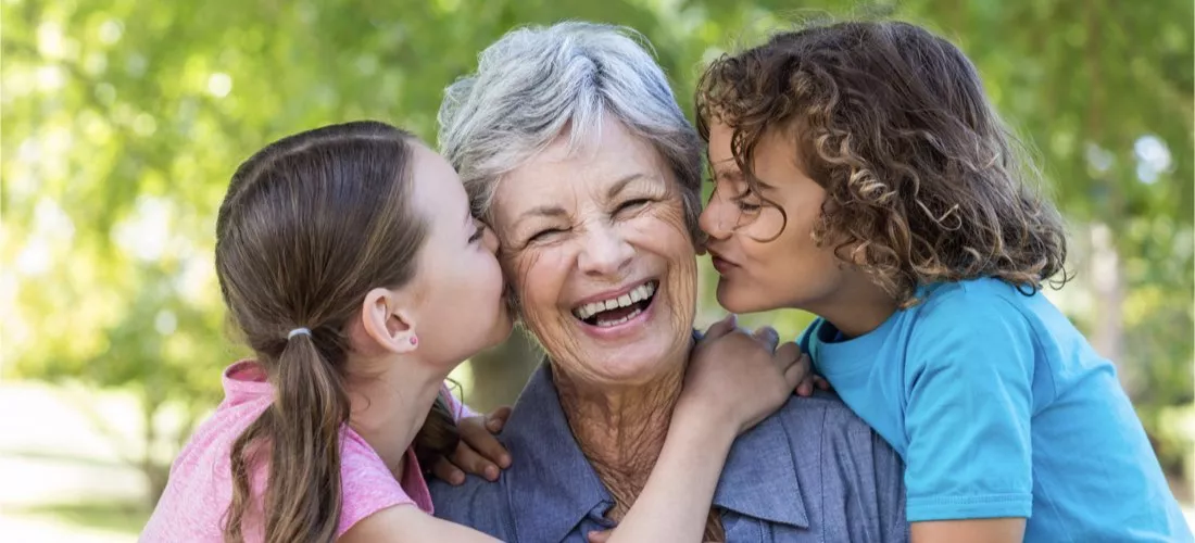 An elderly lady with two children on either side of her giving her a kiss.