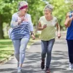 Three elderly woman laughing as they walk down a path together.