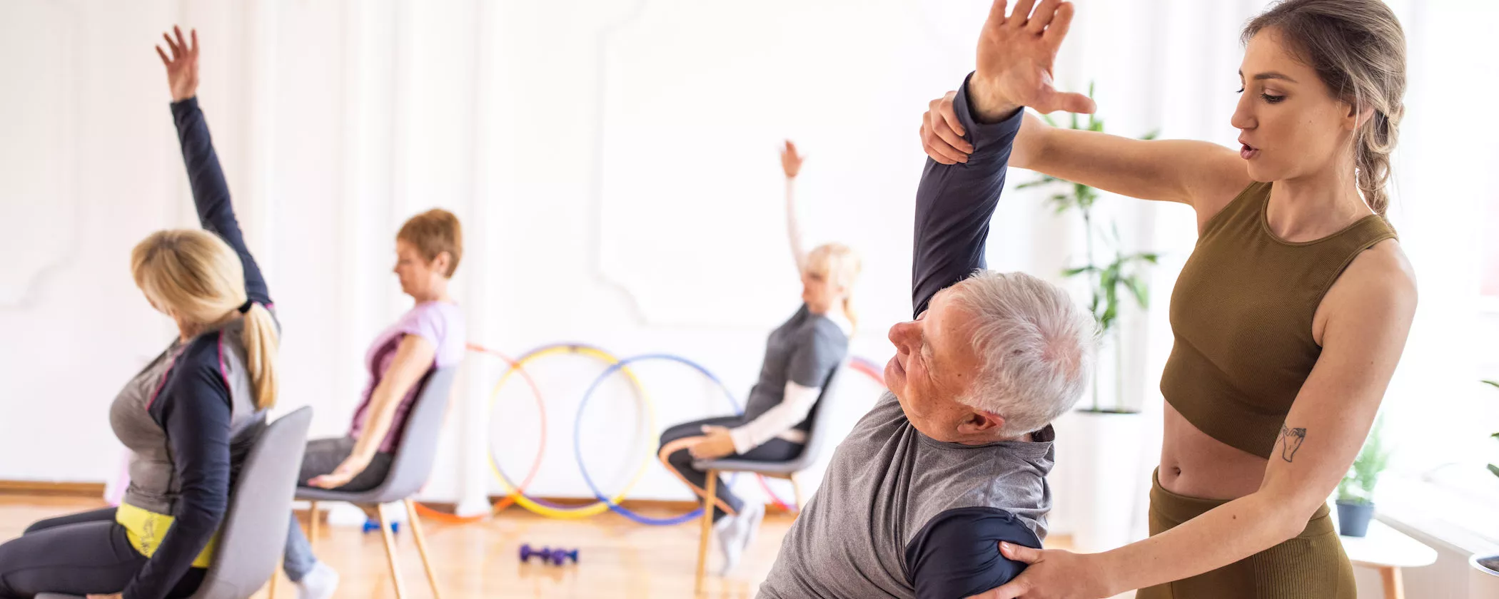 Yoga instructor assisting senior man during yoga class on chairs